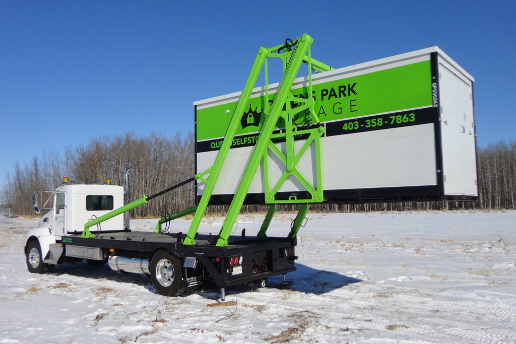 Truck loading green storage container in snowy field.