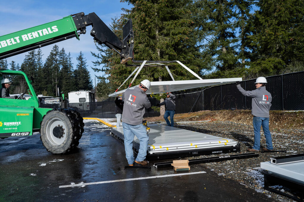 Workers installing large metal sheet with forklift.